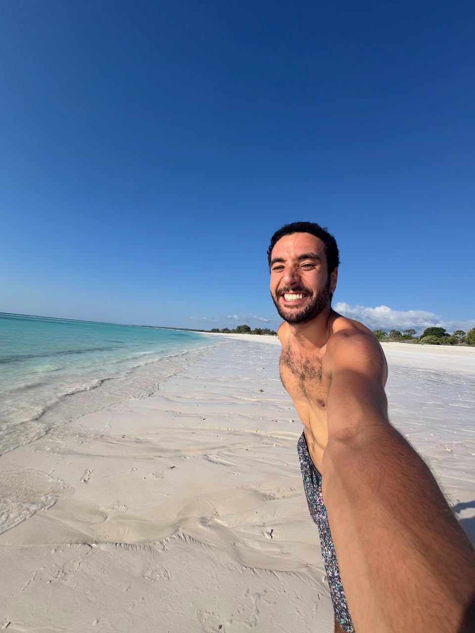 Smiling traveller taking a selfie on a white-sand beach with turquoise water and blue sky